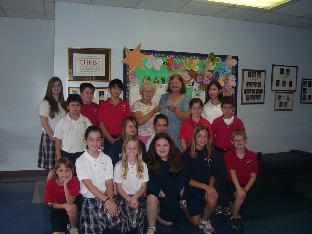 Sheila Harrison, president of Ladies of Sacred Heart, presents a check for $1,200 to Jan Cash, principal at Our Lady of Fatima Catholic School in Benton, AR. The money will be used to update the language arts text books for grades K thru 8. Seventh grade and Fourth grade students in the picture represent the children who will benefit from this donation.